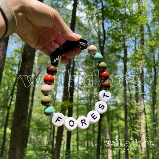 ustom beaded dog collar with earthy forest‑tone beads and FOREST name letters, personalized handmade pet collar by Willadore Collar Co. in a woodland setting