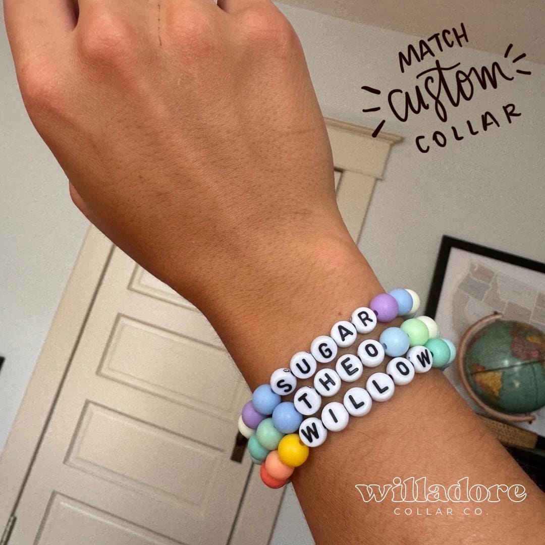 Wrist wearing pastel beaded name bracelets reading SUGAR, THEO, and WILLOW, showing matching accessory options for Willadore Collar Co.’s personalized beaded dog collars