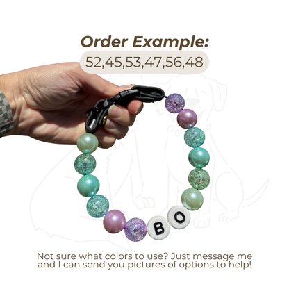 Hand holding a custom beaded dog collar example with purple, teal, turquoise, and glitter beads plus name beads, showing a specialty color order for Willadore Collar Co
